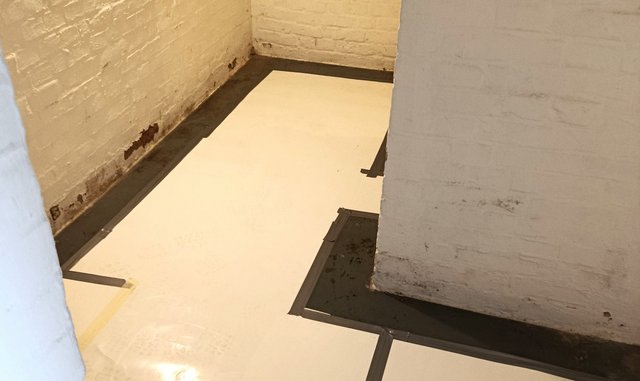 Helle Platten auf Kellerboden verlegt, schwarze Masse am Wandanschluss sichtbar