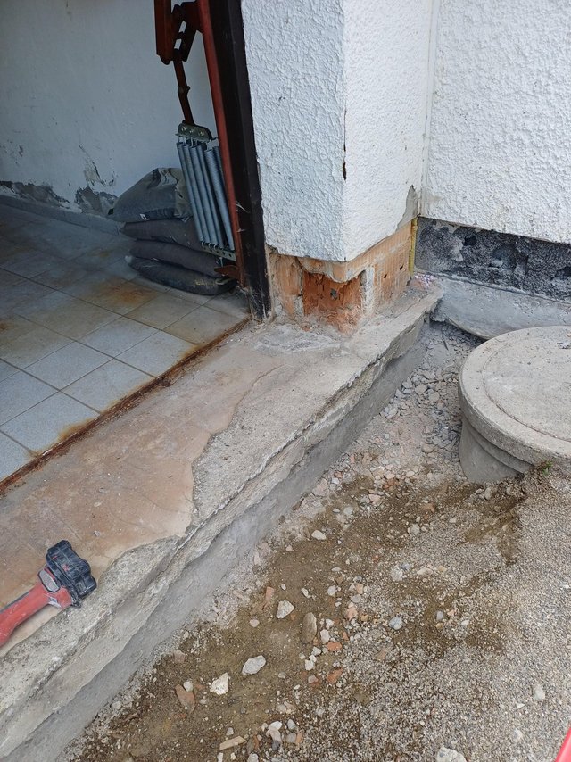 Abgeplatzter Sockelputz an Gebäudeecke, freiliegendes Mauerwerk am Betonpodest