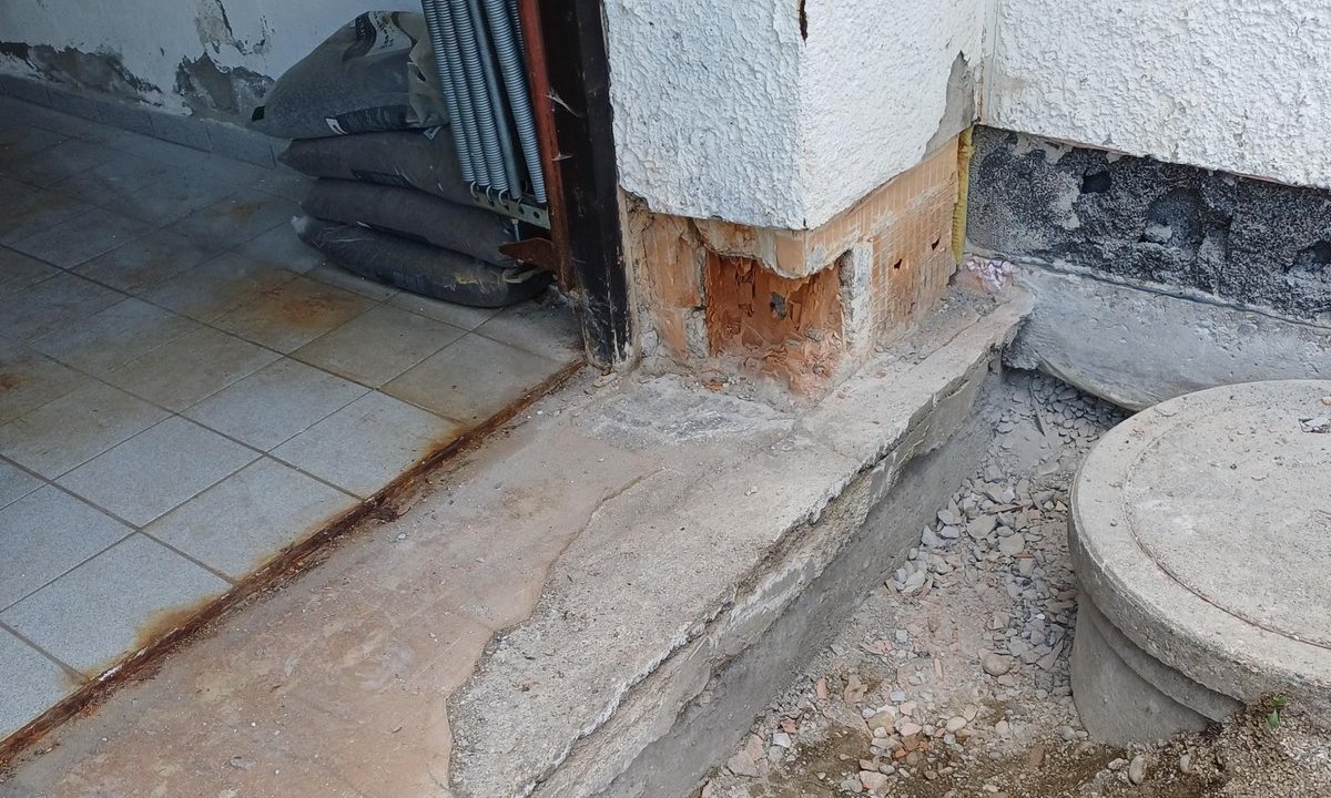Abgeplatzter Sockelputz an Gebäudeecke, freiliegendes Mauerwerk am Betonpodest