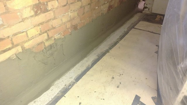 Ziegelmauer mit aufgetragener grauer Masse im Sockelbereich, Boden mit Platten.