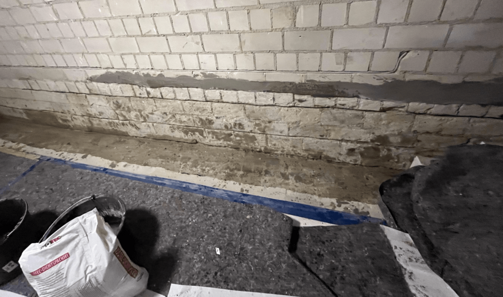 Verschmutzte Kellerwand aus weißen Ziegeln, graue Masse entlang der Fugen.