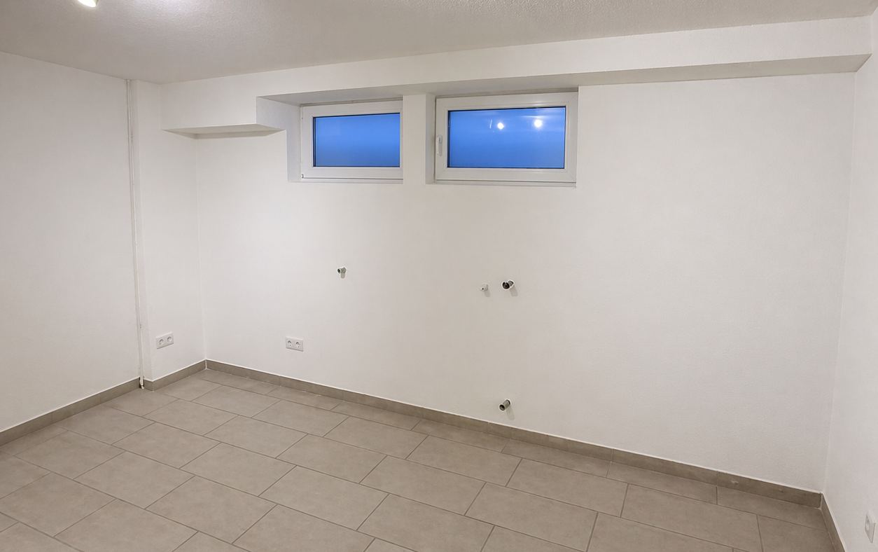 Leerer Raum mit Fliesenboden, zwei kleinen Fenstern und Deckenstrahlern