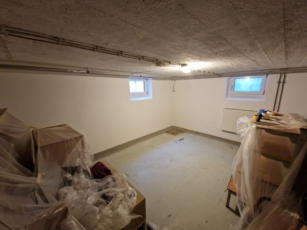 Leerer Kellerraum mit weißen Wänden, Beton­decke und abgedeckten Möbeln