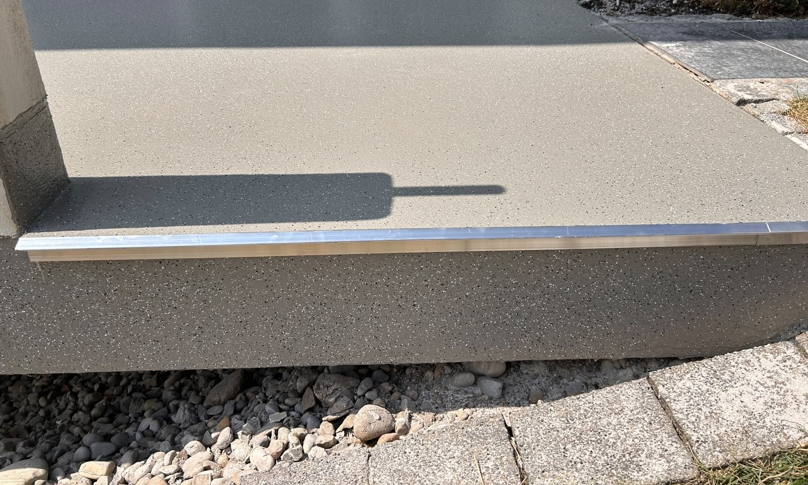Grauer, gesprenkelter Balkonboden vor Fenstertür mit Metallschiene am Rand
