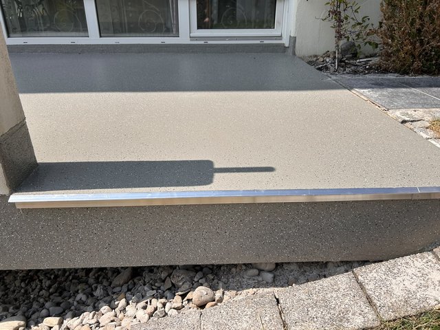 Grauer, gesprenkelter Balkonboden vor Fenstertür mit Metallschiene am Rand