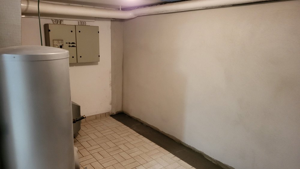 Kelleraum mit heller Wand, Rohrleitungen und Bodenfliesen