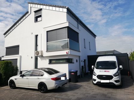 Modernes Wohnhaus mit Parkplatz, ISOTEC Transporter und silbernem Auto vor der Einfahrt.