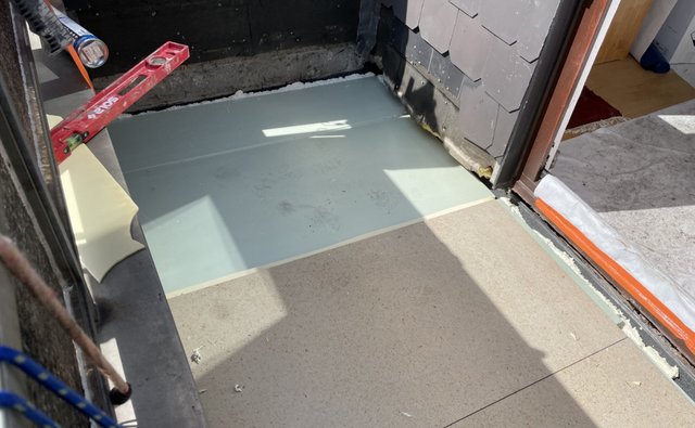 Helle Platte auf Balkonboden an Türschwelle, daneben Wasserwaage