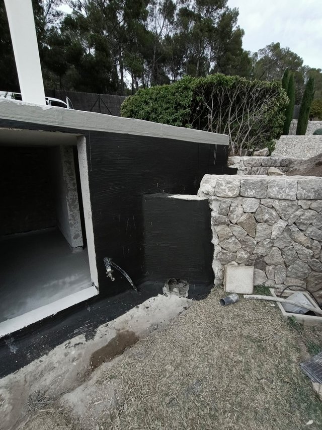 Schwarze Masse auf Betonkonstruktion neben Natursteinmauer, Außenaufnahme