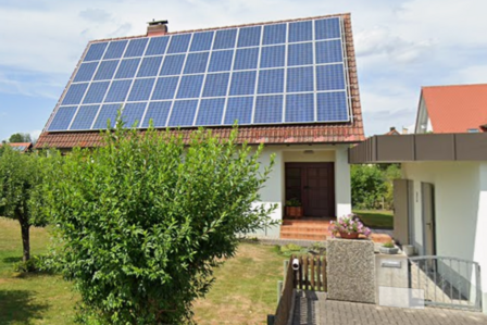 Einfamilienhaus mit Solarmodulen auf dem Ziegeldach, Vorgarten mit Baum.