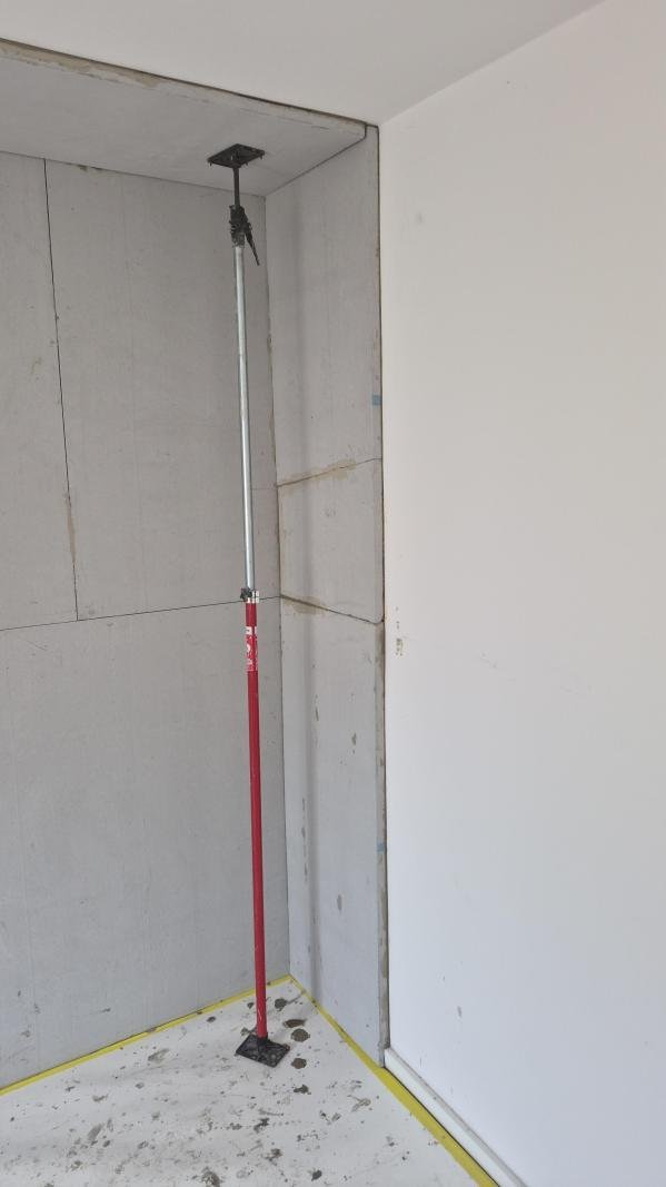 Stütze fixiert helle Platten an Zimmerecke während der Montage.