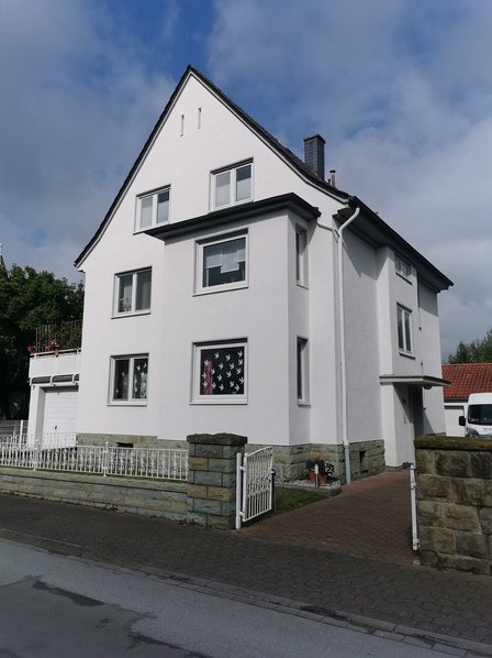 Weißes Wohnhaus mit Satteldach und Vorgartenzaun vor strahlend blauem Himmel