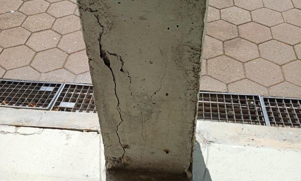 Rissiger Betonpfeiler auf Gehweg, Nahaufnahme mit Schadstellen am Sockel