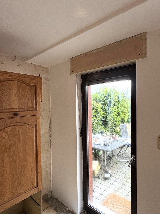 Tür mit Fenster, daneben freigelegte Wandkante und montierte Platte über dem Rahmen.