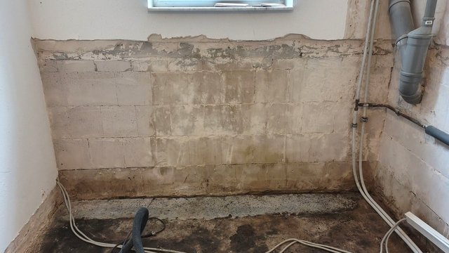 Freigelegte Kellerwand aus Kalksandstein mit dunklen Feuchteflecken, rechts Rohrleitungen