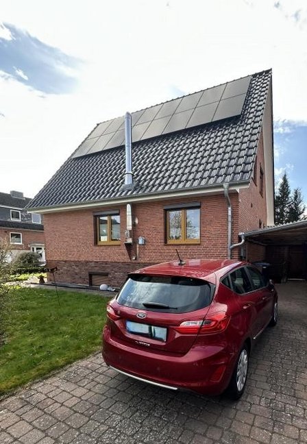 Einfamilienhaus mit Solarmodulen auf dem Dach, rotes Auto auf gepflasterter Einfahrt.