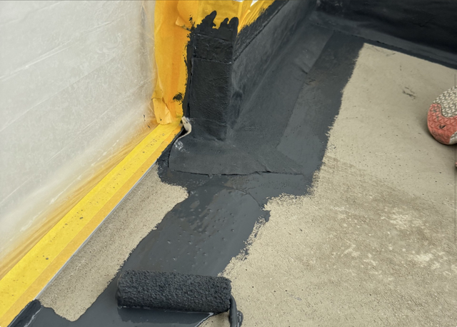 Schwarze Masse wird am Boden und Sockelbereich aufgetragen, Nahaufnahme