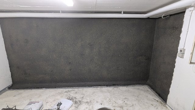 Dunkle Kellerwand mit schwarzer Masse, Rohrleitung unter der Decke.