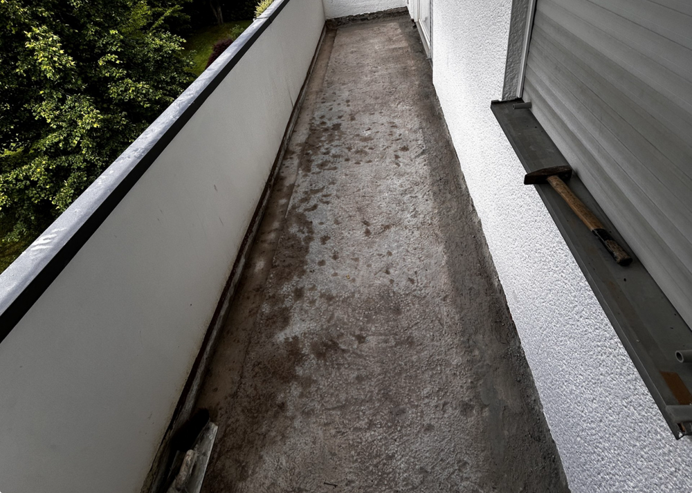 Balkon mit freigelegtem Betonboden und Hammer auf Fensterbank