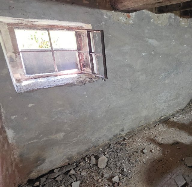 Kleines geöffnetes Fenster in rauer grauer Kellerwand, Bauschutt am Boden