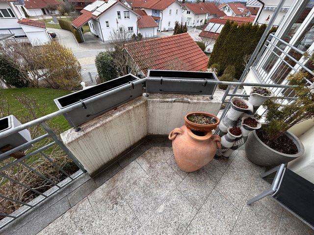 Balkon mit grauen Blumenkästen am Geländer, Pflanzgefäßen und Blick auf Wohnhäuser mit Ziegeldächern