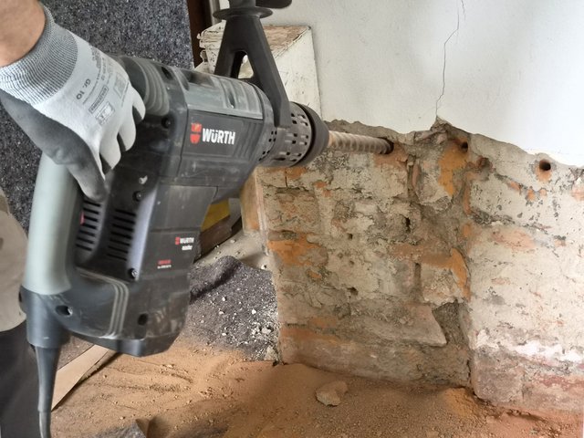 Arbeiter bohrt Löcher in freigelegtes Mauerwerk mit Bohrhammer.