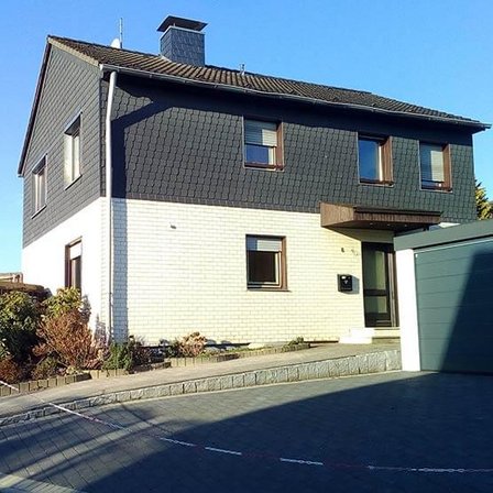 Zweistöckiges Wohnhaus mit heller Klinkerfassade und dunkler Schieferverkleidung.