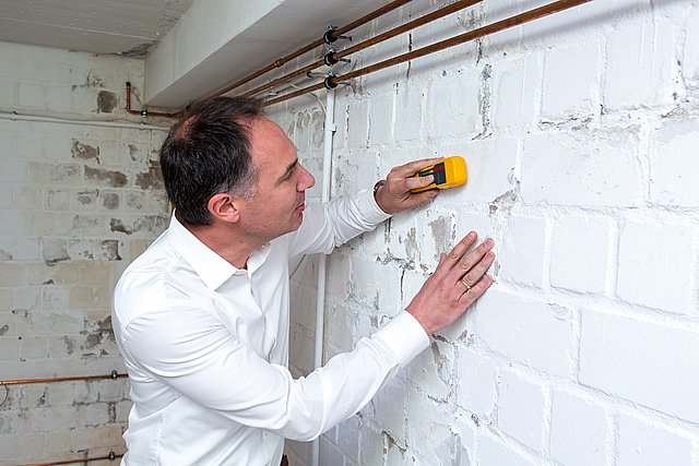 Person misst beschichtete Ziegelwand mit Handgerät
