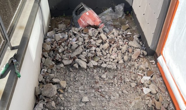 Bauschutt und aufgebrochener Beton auf schmalem Balkon, daneben Abbruchhammer