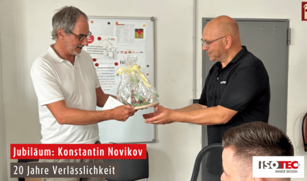 ISOTEC Mitarbeiter überreicht Geschenkkorb im Büro, Text „Jubiläum: Konstantin Novikov“.