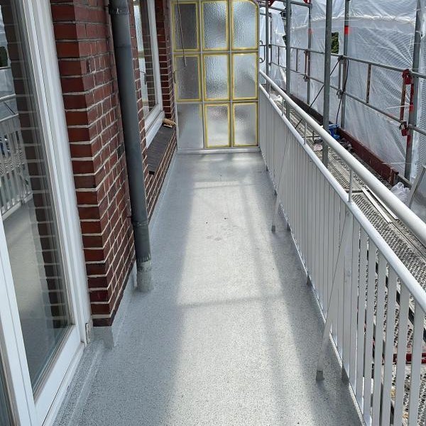 Balkon mit frischem grauem Bodenbelag, Geruest und Schutzfolie entlang der Fassade