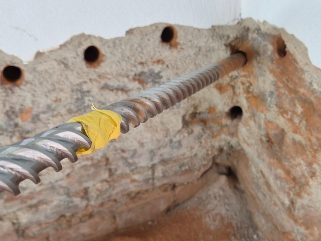 Spiralförmiger Bohrer ragt in ein Bohrloch einer rauen Mauer mit mehreren Bohrlöchern.