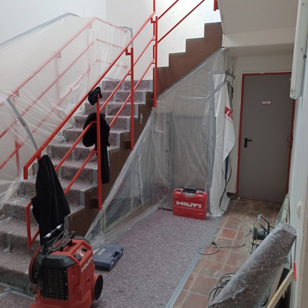 Abgeklebtes Treppenhaus mit Folienabdeckung, roten Geländern und Baugeräten am Boden