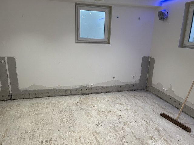 Heller Kellerraum mit freigelegtem Boden und grauer Masse entlang der Wand