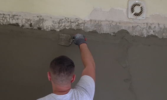 Arbeiter trägt graue Masse mit Kelle auf Wand im Raum auf