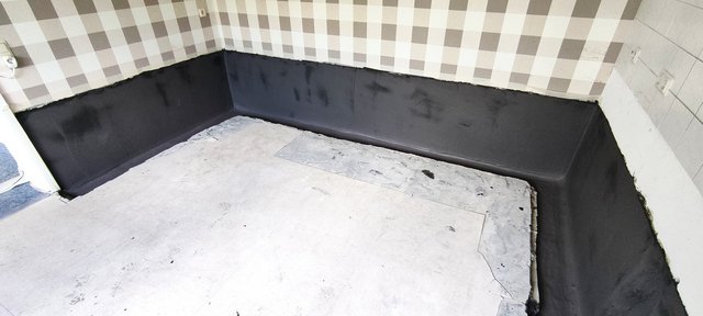 Schwarze Masse auf unterem Wandbereich in leerem Raum.