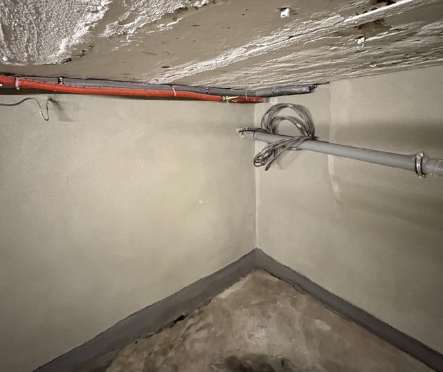 Kellerraum mit heller Wandbeschichtung, grauem Sockelstreifen und Leitungen an der Decke