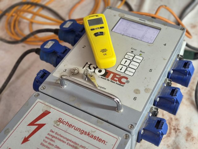 ISOTEC Steuergerät mit Kabeln und gelbem Messgerät auf Baustellenboden