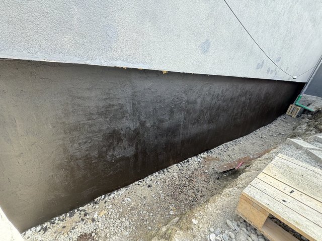 Dunkle Masse auf Außenwand über freigelegtem Fundament