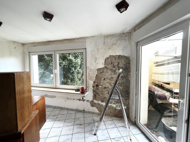 Freigelegte Mauerstelle mit beschädigtem Putz in Zimmer neben Fenster und Balkontür