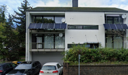 Modernes Wohnhaus mit Balkon und Solarpaneelen an der Fassade, Autos davor