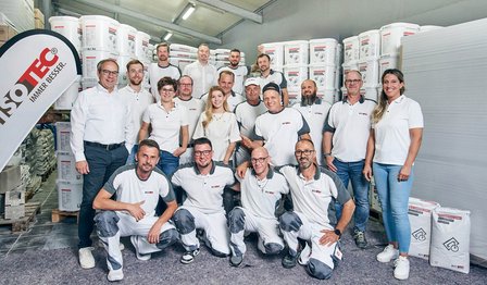 ISOTEC Team posiert in Lagerhalle vor Eimern und Säcken mit Baumaterial