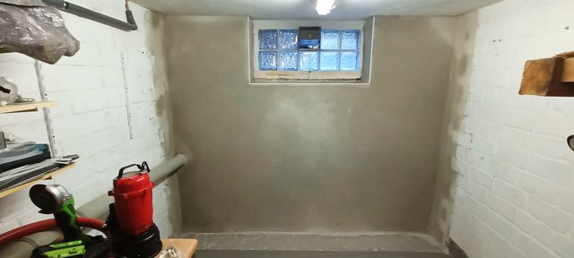 Beschichtete graue Wand mit Glasbausteinfenster in einem Kellerraum