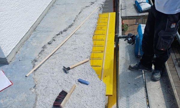 Arbeiter entfernt graue Balkonbeschichtung, Werkzeuge und Geruestbelag neben Balkonkante