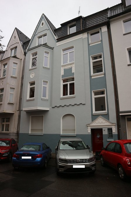 Blau-graue Hausfassade mit Giebeln und geparkten Autos vor dem Eingang