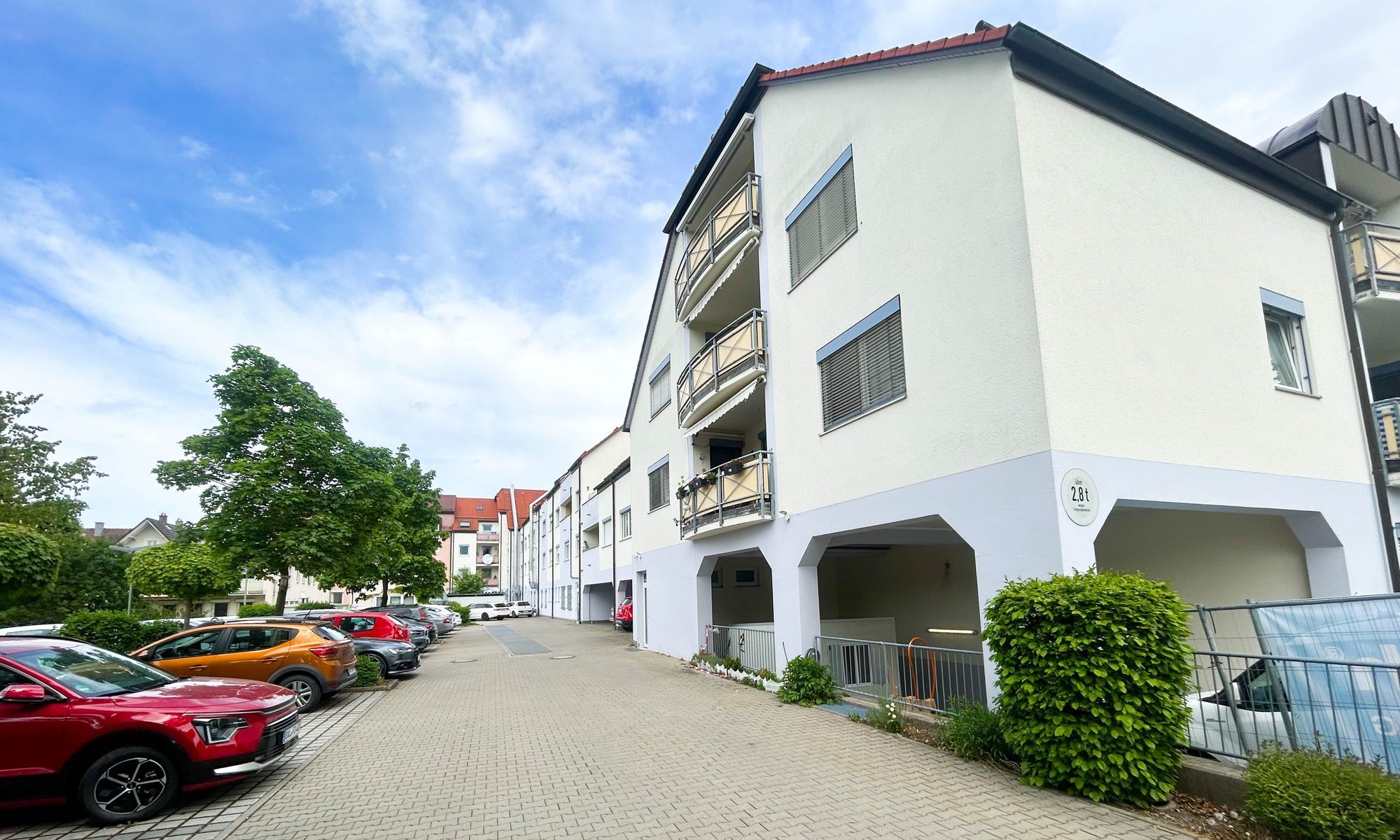 Mehrfamilienhaus mit Balkonen, gepflasterter Zufahrt und parkenden Autos