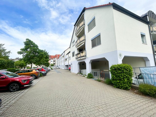 Mehrfamilienhaus mit Balkonen, gepflasterter Zufahrt und parkenden Autos