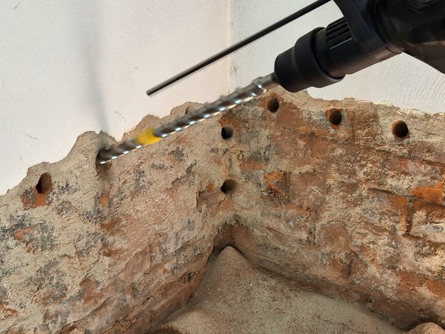Bohrmaschine bohrt Löcher in freigelegte Ziegel- und Mörtelfläche in Raumecke