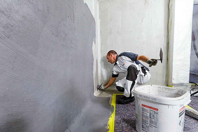 ISOTEC Mitarbeiter trägt graue Masse auf Wand‑Boden‑Übergang auf