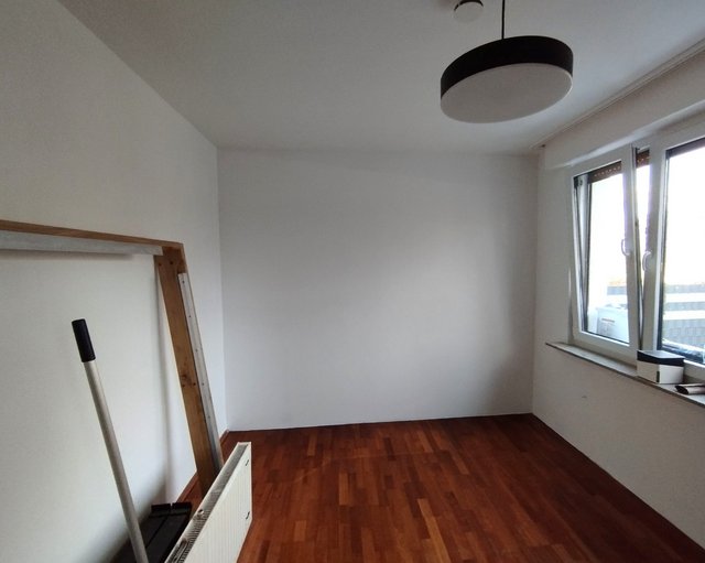 Leerer Raum mit Holzfußboden, weißen Wänden und Fensterfront